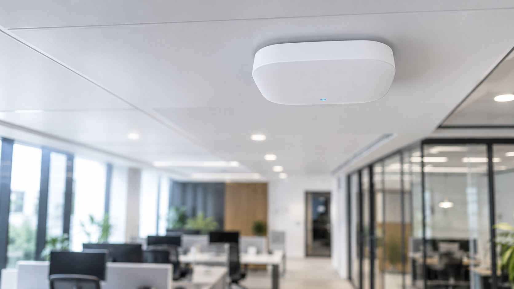White ceiling-mounted wireless access point above an open-plan office
